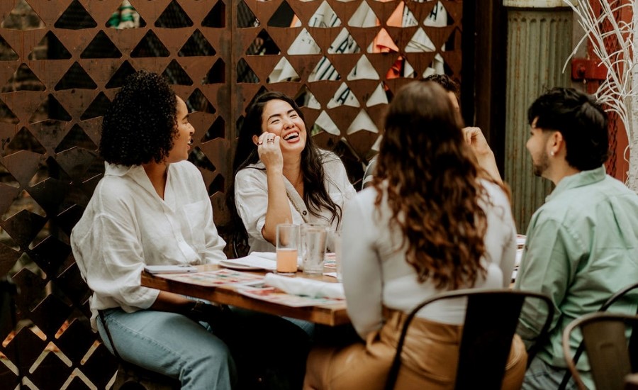 Freund:innen sitzen an einem Tisch und lachen.