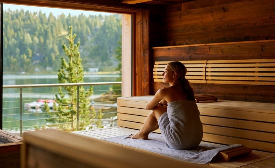 Frau in Sauna mit Blick auf See und Wald
