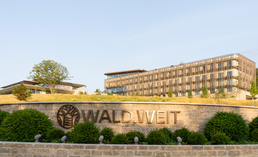 Wald.Weit Außenansicht: Modernes Hotelgebäude in Holzoptik mit Logo und Natursteinmauer im Vordergrund, eingebettet in die Landschaft des Rheingaus.