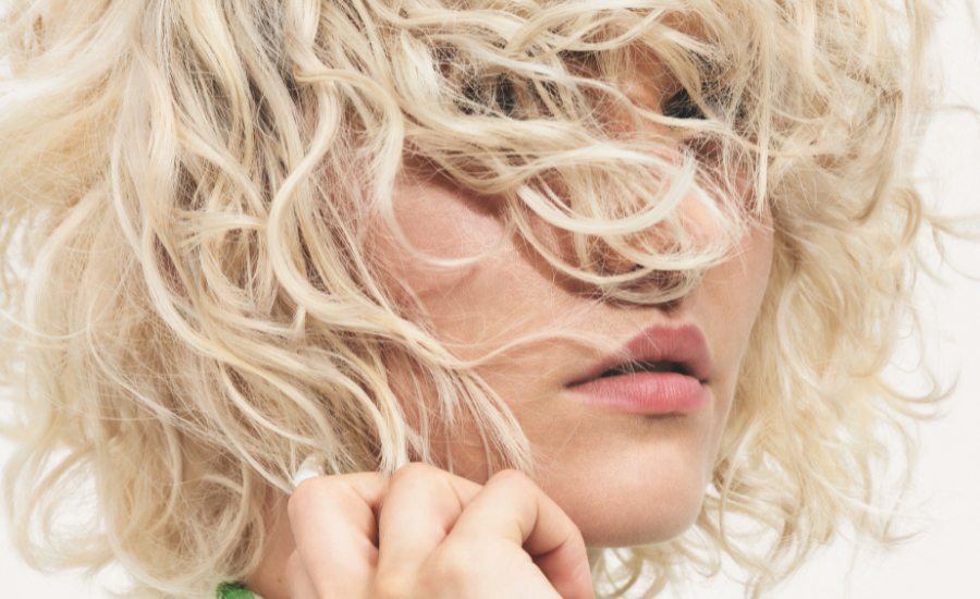 Schwarzkopf Professional Aufmacherbild mit Nahaufnahme von blond gelocktem Haar, das teilweise ins Gesicht fällt, Lippen in sanftem Roséton.