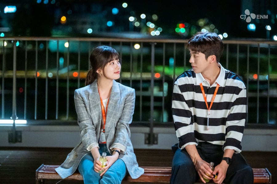 Szene aus dem K-Drama „Start-Up“: Zwei junge Erwachsene sitzen nachts auf einer Bank und schauen sich an; im Hintergrund leuchten unscharfe Stadtlichter.