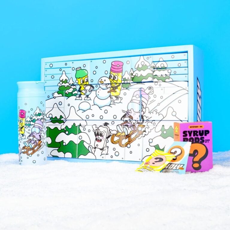 Hellblauer Holy-Adventskalender mit Comic-Winterszene, daneben eine Trinkflasche und Sirup-Pods im Schnee