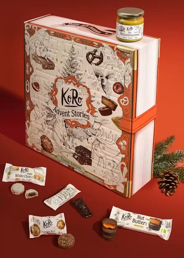 Adventskalender „Advent Stories“ von KoRo in Buchoptik, davor Riegel, Pralinen und ein Glas Pistaziencreme