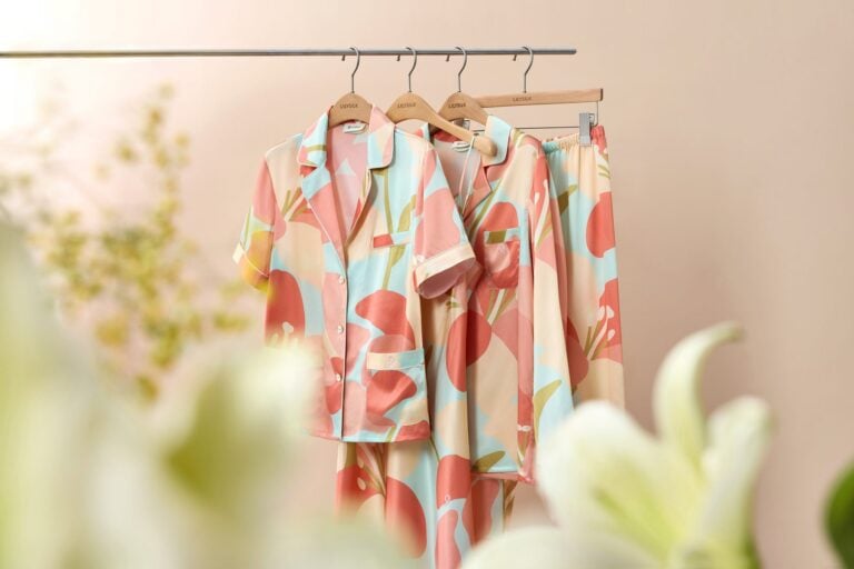 Seidenpyjamas mit großem Blütenmuster in Rosa, Koralle und Mint hängen an einer Kleiderstange