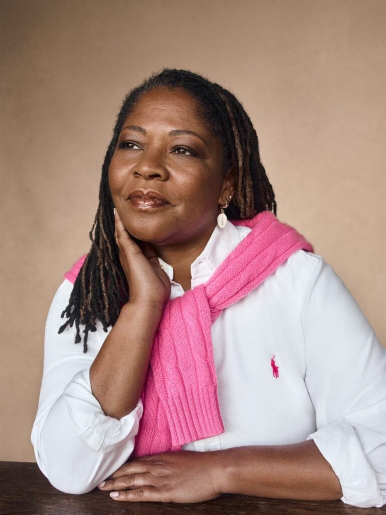 Frau mit Locs in weißer Bluse und pinkem Pullover über den Schultern