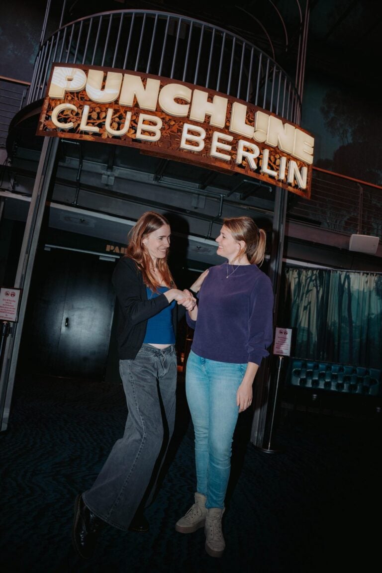 Zwei Frauen unterhalten sich unter dem leuchtenden Schriftzug Punch Line Club Berlin