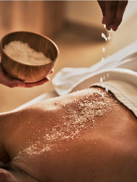 Iberostar Selection Es Trenc: Salzpeeling wird sanft auf dem Rücken einer Person aufgetragen – Wellnessanwendung mit natürlichen Essenzen im Spa-Bereich des 5-Sterne-Hotels auf Mallorca.